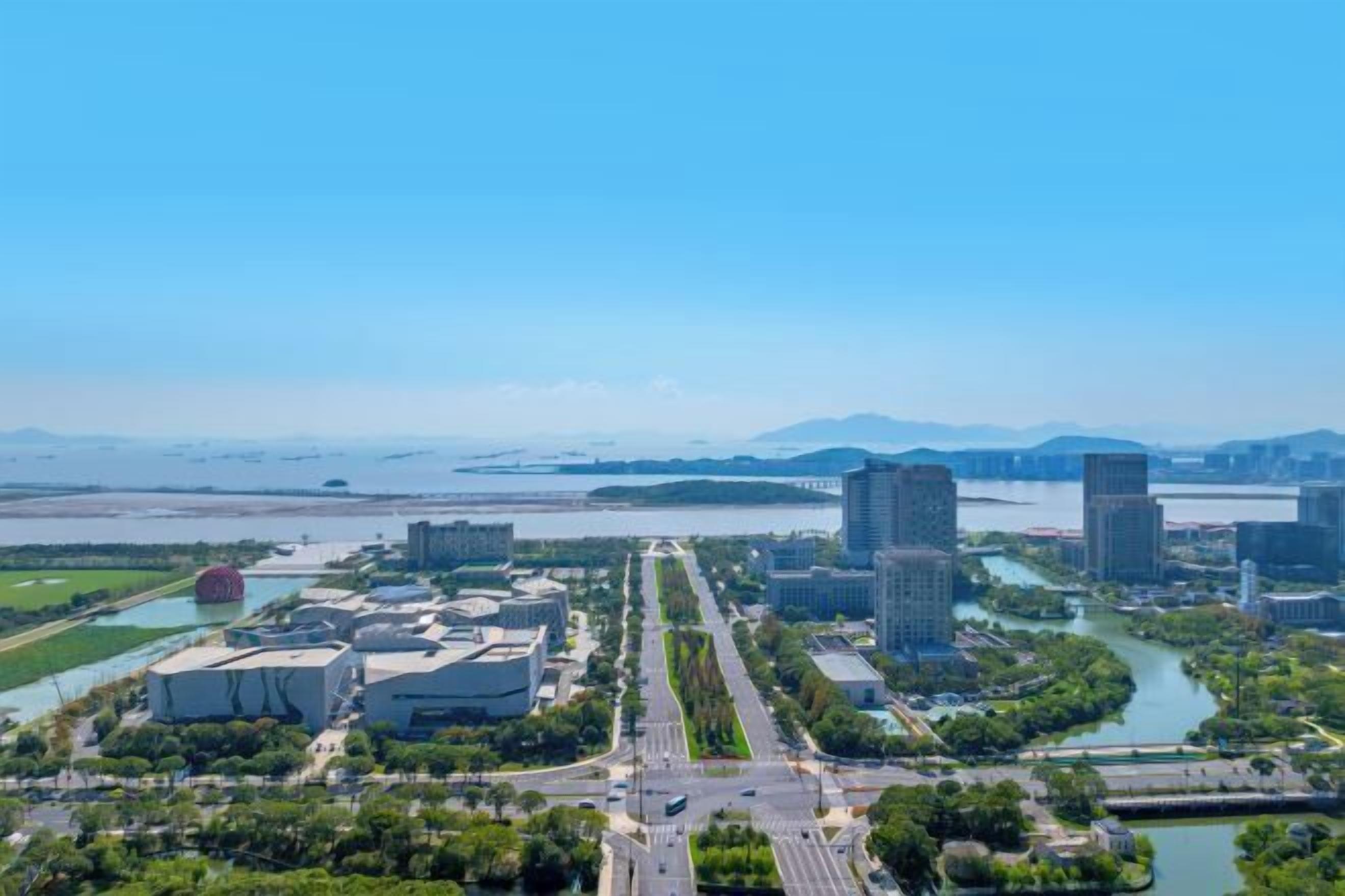 An aerial view of a cityscape with modern buildings, a river, and a bridge.