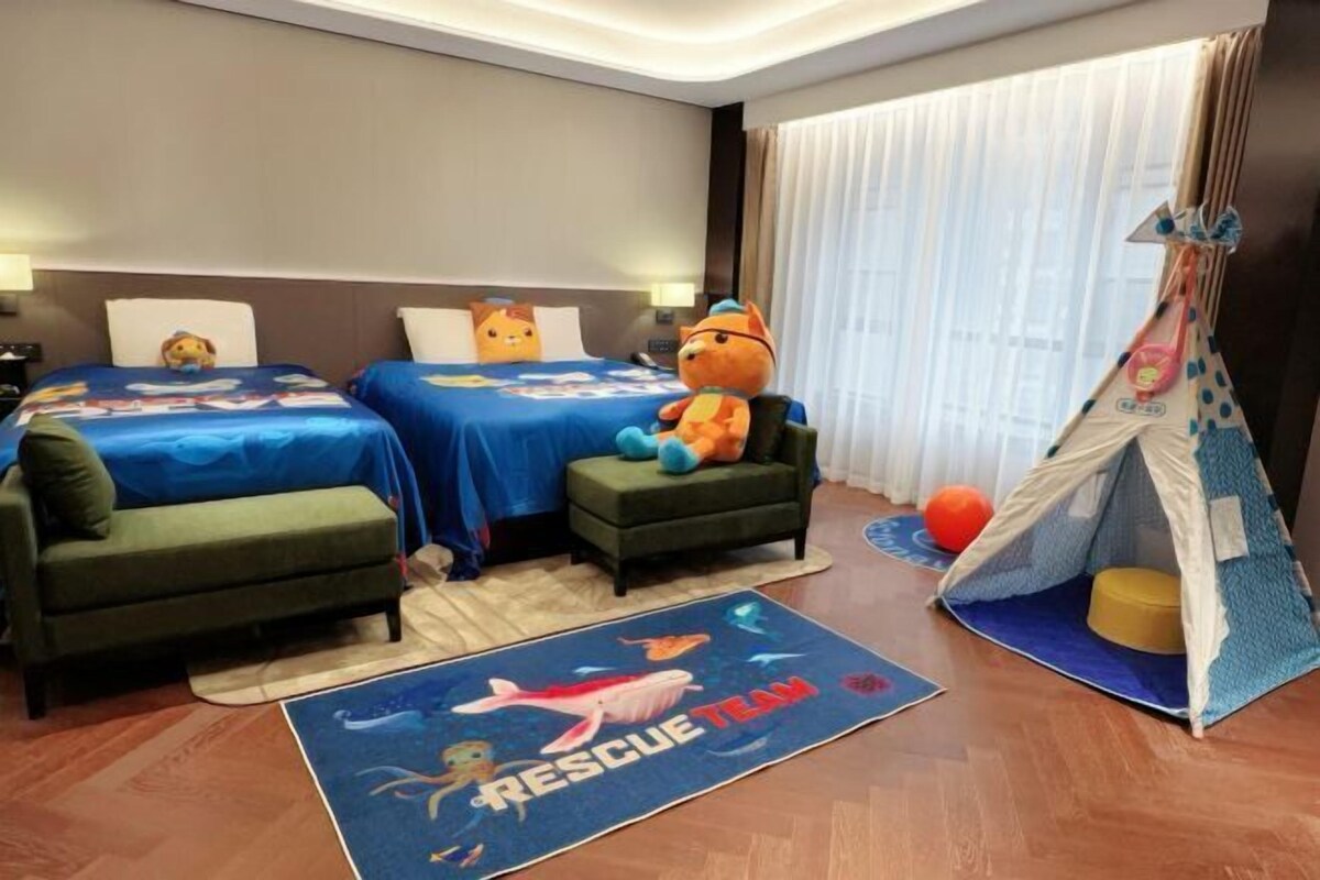 A hotel room with two beds, a green sofa, a tent, and a 'Rescue Team' themed rug.