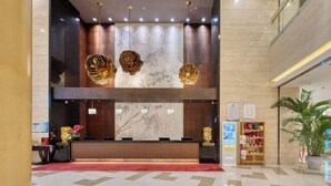 Zona de recepción de un hotel con mostrador de mármol, paneles de madera y alfombra roja.