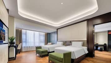 A hotel room with two beds, a desk, a chair, and a small green sofa.
