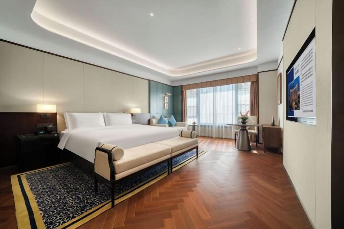 A modern hotel room with a large bed, a sofa, a desk, and a view of the outdoors.
