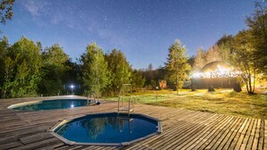 Une terrasse en bois avec une piscine, entourée d’arbres et bordée d’un bâtiment doté d’un toit en verre.