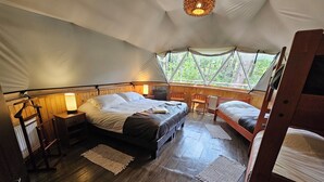 Une chambre d’hébergement sous tente comprenant un grand lit, un lit plus petit, un bureau et une chaise.
