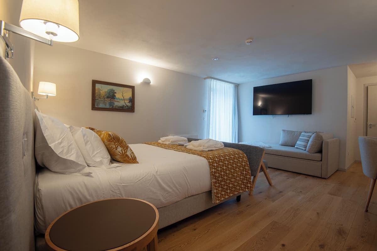 A hotel room with a bed, a sofa, a TV, and a painting on the wall.