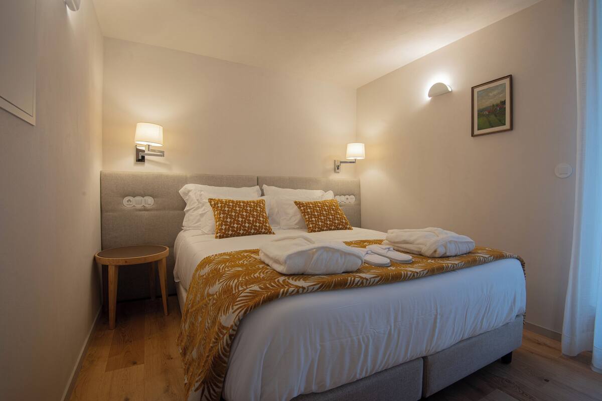 A hotel room with a large bed, two bedside lamps, a small table, and a framed picture on the wall.