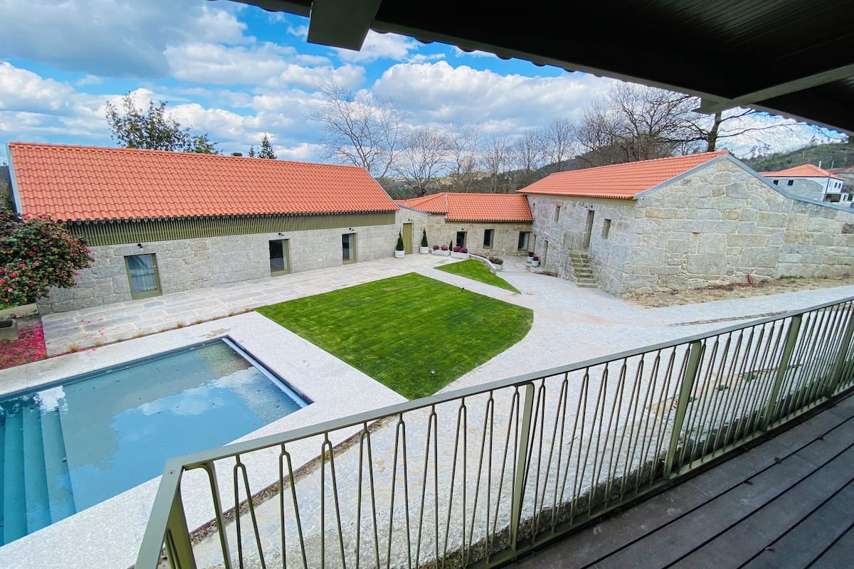 A courtyard with a swimming pool, stone buildings with red roofs, and a grassy lawn.