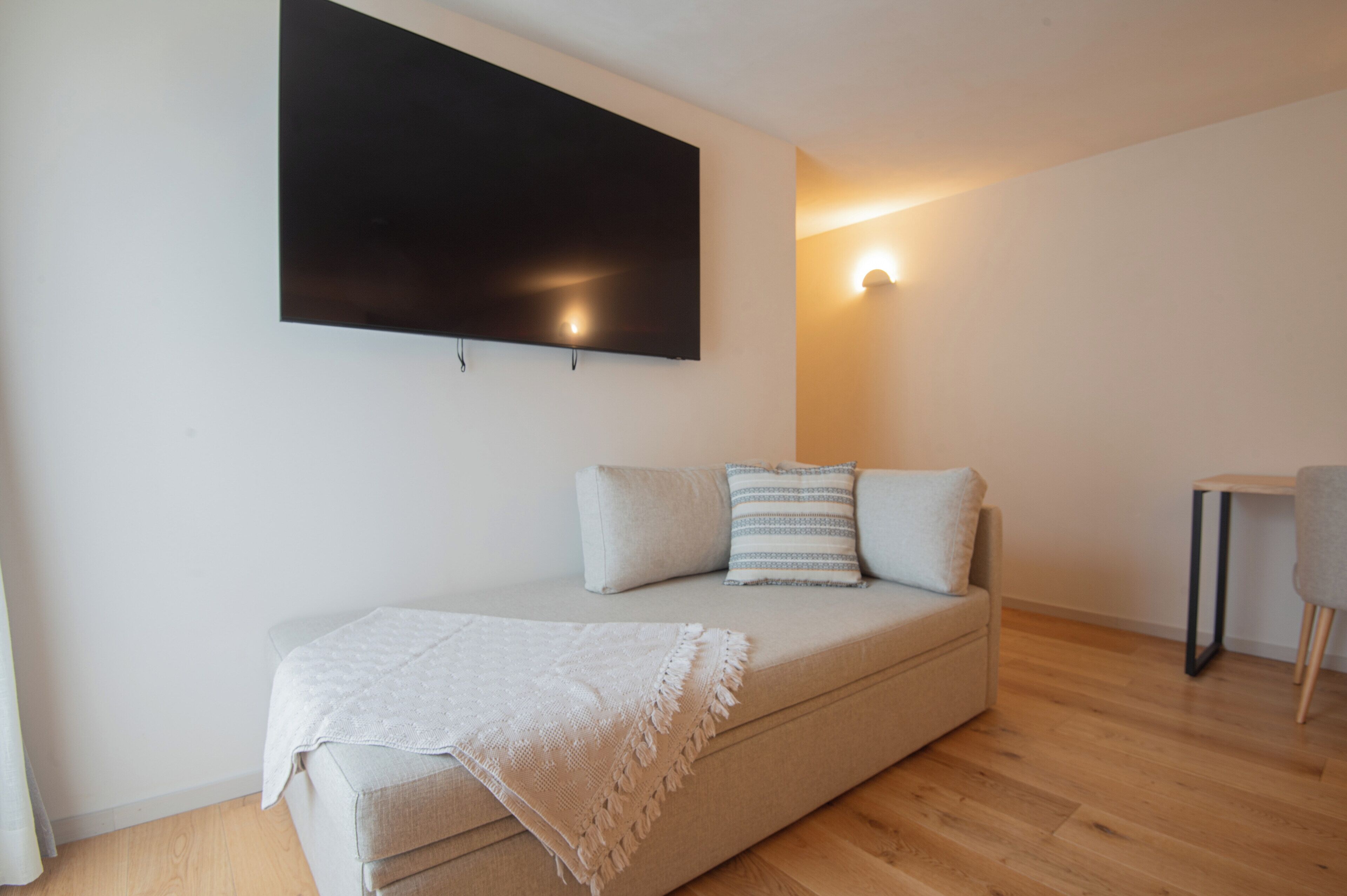 Un salon moderne avec un canapé, un téléviseur à écran plat fixé au mur et une petite table avec une chaise.
