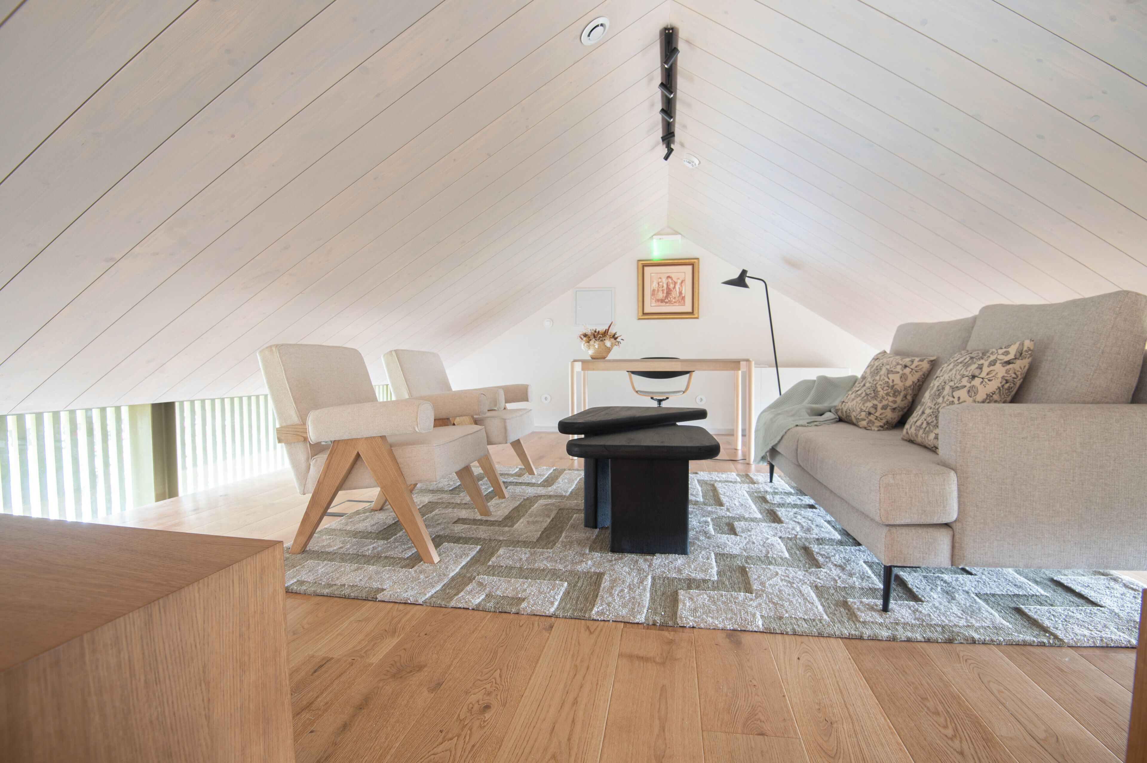 A modern loft bedroom with a sloped ceiling, a sofa, a chair, a small table, and a floor lamp.