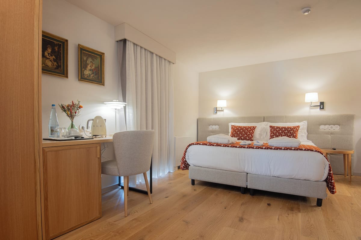 A hotel room with a bed, a desk, a chair, a lamp, and a picture on the wall.