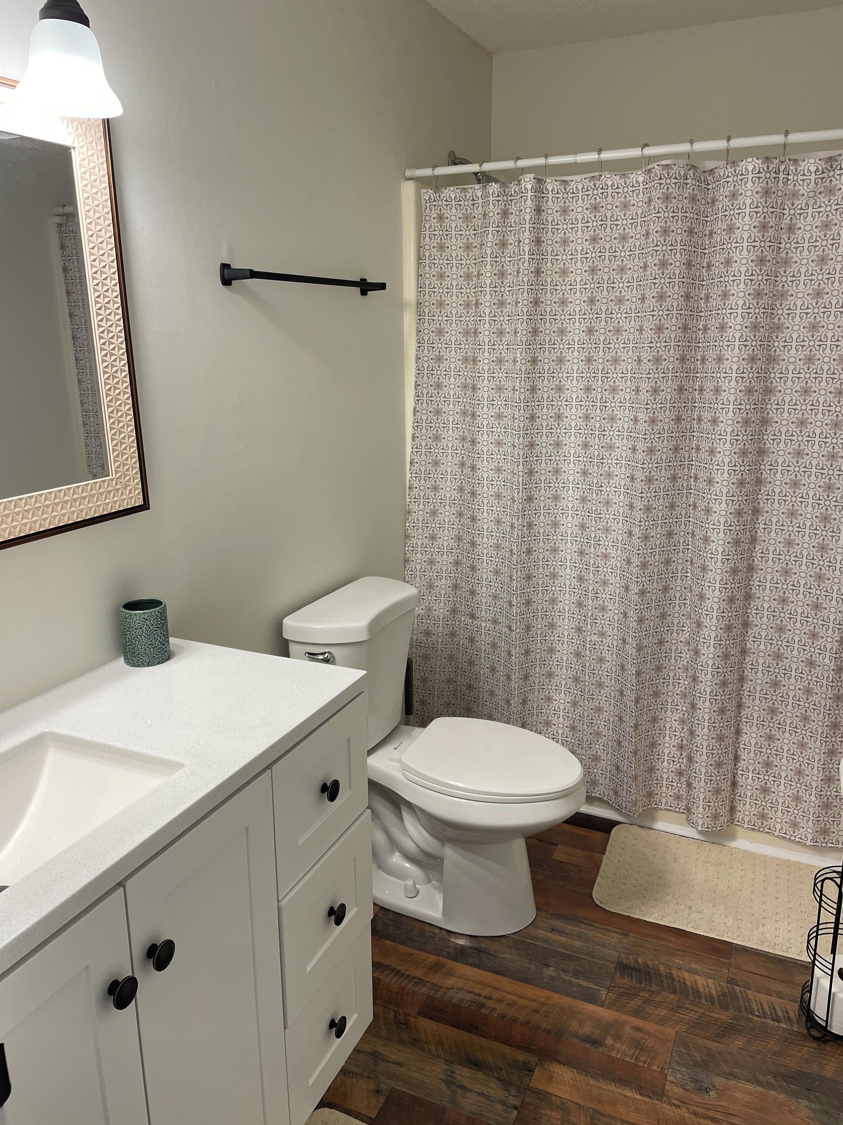 Une salle de bain avec un lavabo blanc, des toilettes, un rideau de douche et un miroir doté d’un cadre géométrique.