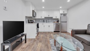A modern kitchen with white cabinets, a microwave, and a dishwasher. There is a glass table and a grey sofa in the living area. - Luxury 2Bdr Retreat, Calgary,  Everything You Need, Best coffee (Calgary)