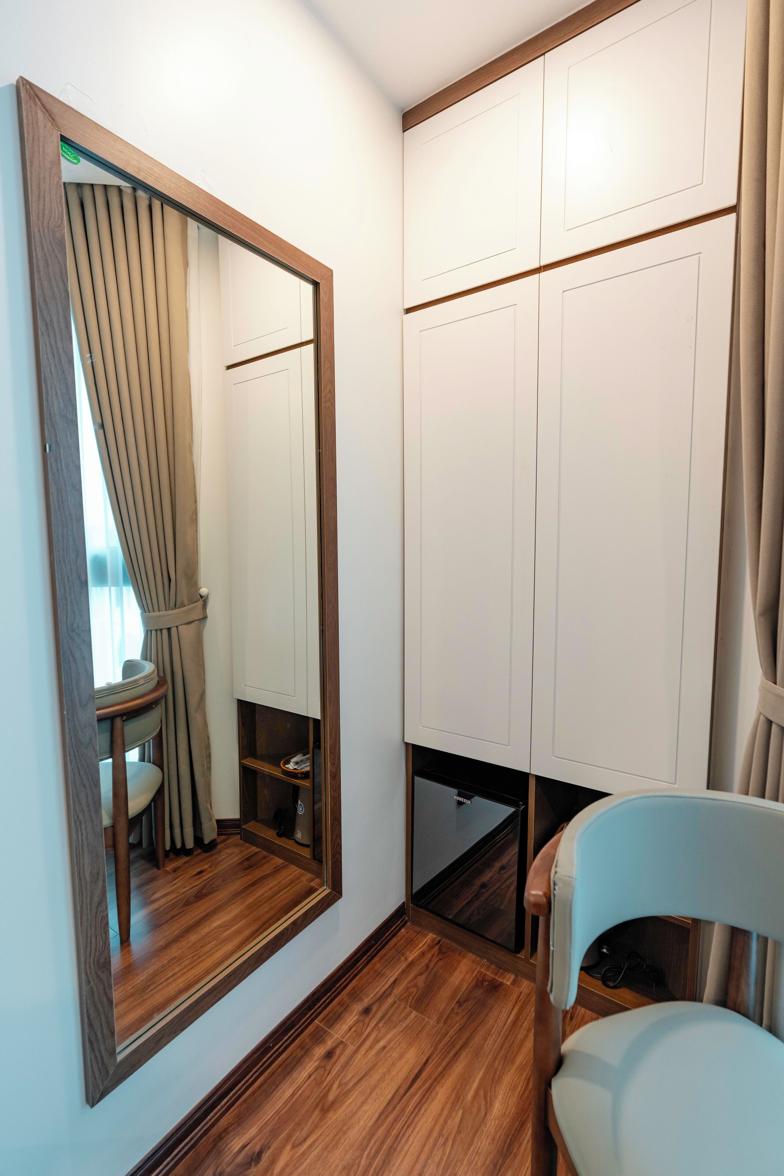 A room with a large mirror, wooden flooring, a chair, and a wardrobe with multiple doors.