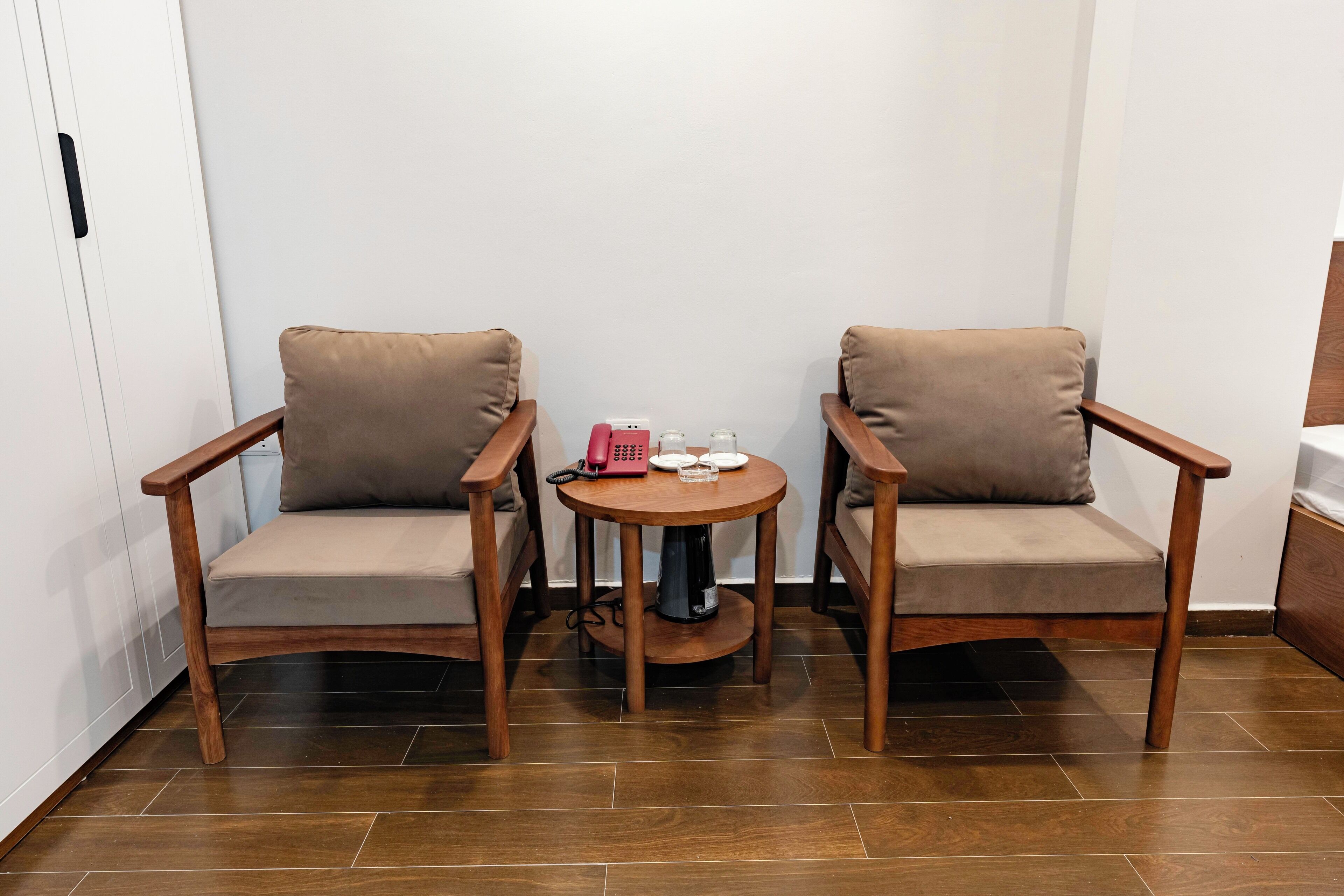 Una habitación con dos sillas de madera con cojines, una mesita redonda con un teléfono, vasos y una tetera.