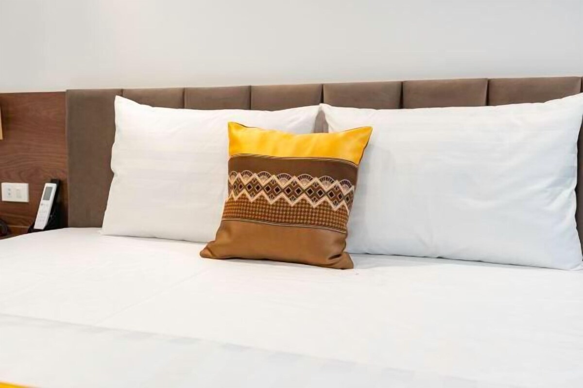 A bed with white bedding and a decorative pillow with a geometric pattern.