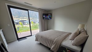 Habitació d'hotel amb un llit, una televisió penjada a la paret, una porta corredissa de vidre que dona a una zona exterior i una taula petita amb una planta.