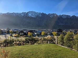 A residential area with houses, a grassy foreground, and snow-capped mountains in the background.