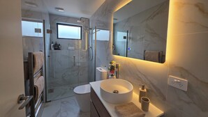 Un bany modern amb dutxa de vidre, un mirall gran, un lavabo rodó i un vàter.