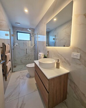 Une salle de bain moderne avec une douche à parois de verre, des toilettes et un meuble-lavabo avec un miroir.
