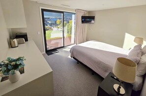Une chambre d’hôtel équipée d’un lit, d’un téléviseur fixé au mur, d’un bureau avec une lampe et offrant une vue sur l’extérieur grâce à une porte coulissante.