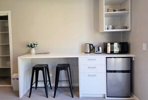 A compact kitchenette with a white countertop, two black stools, a stainless steel refrigerator, and a microwave. - Loop the Loop (Queenstown)