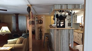 A cozy living room with a sofa and a table, a kitchen with hanging pots, and a wooden wall.