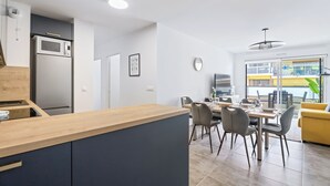 A modern kitchen with a wooden countertop, a built-in microwave, and a refrigerator. There is a dining area with a table and chairs, and a yellow sofa. - Appartement Amandiers - Welkeys (Cagnes-sur-Mer)