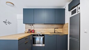 A modern kitchen with dark blue cabinets, a stainless steel oven, and a built-in microwave. - Appartement Amandiers - Welkeys (Cagnes-sur-Mer)