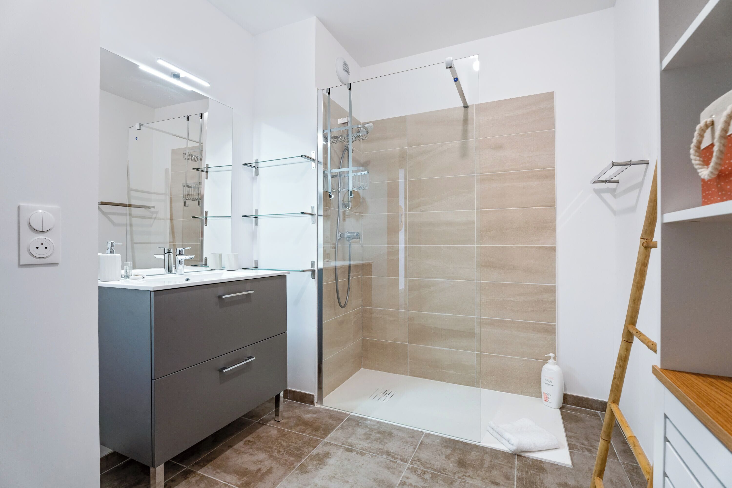 A modern bathroom with a glass shower enclosure, a vanity with a mirror, and a wooden ladder.