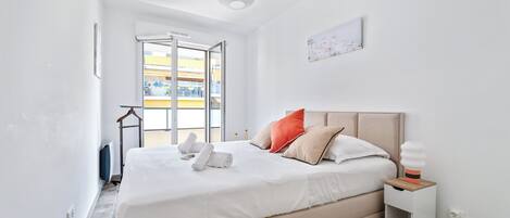 A modern bedroom with a large bed, a bedside table, a hanging light, and a view of the outside balcony.