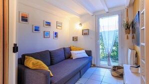 Ein modernes Wohnzimmer mit grauem Sofa, gelber Tagesdecke und gerahmten Bildern an der Wand.