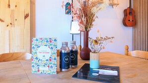 Ein Holztisch mit einem Buch, zwei Wasserflaschen, einer Vase mit getrockneten Blumen und einer Gitarre an der Wand.