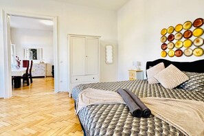 A bedroom with a patterned bedspread, a wooden floor, a wardrobe, and a wall-mounted mirror.