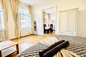 Une chambre à coucher avec un lit, une table et une chaise. On y trouve également une armoire et une porte qui donne sur une autre pièce.