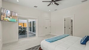 A bedroom with a bed, a ceiling fan, a TV mounted on the wall, and a sliding glass door leading to a patio area. - Welcome to Casa Rio, our spacious house in scenic Jensen Beach! (Jensen Beach)