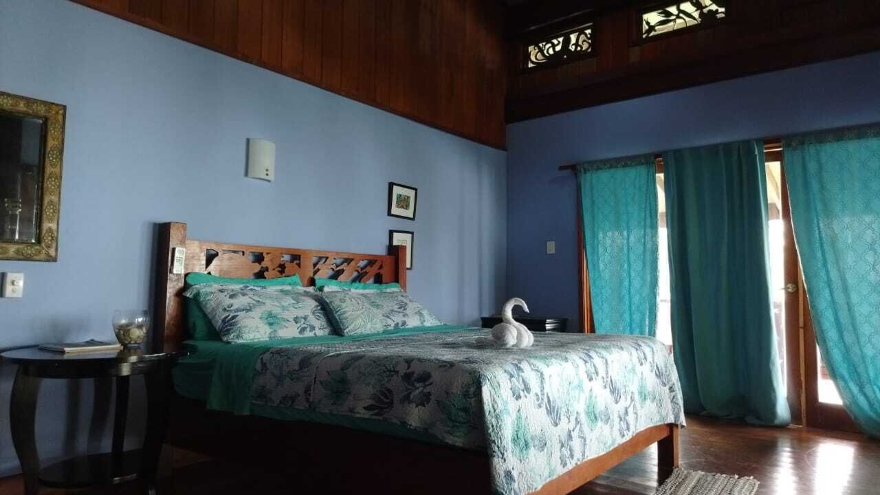 A bedroom with a wooden bed, a bedside table, a wall-mounted light, and a window with curtains.