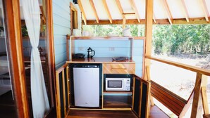 A compact kitchenette with a refrigerator, microwave, and wooden shelves.