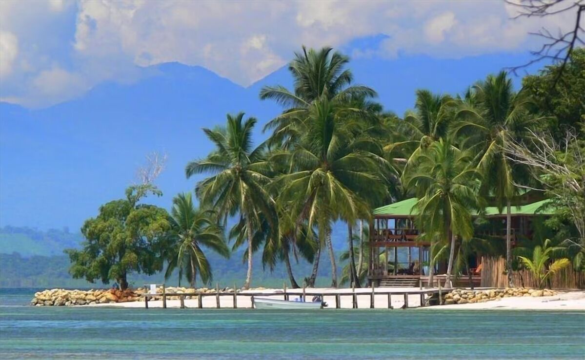A beach with palm trees, a wooden structure, and a mountain in the background.