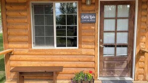 A wooden cabin with a bench outside, a door with a window, and a sign that reads "Cattle Kate". - Cattle Kate At Mountain River Ranch (Ririe)
