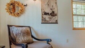 A room with a wooden ceiling, a framed photograph on the wall, a chair with a cushion, and a rug on the floor. - Cattle Kate At Mountain River Ranch (Ririe)