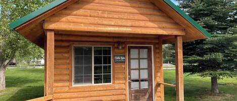 A small wooden cabin with a porch, a bench, and a sign that reads "Cottage Cove."