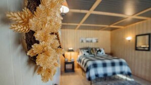 A room with a bed, a nightstand, a lamp, and a wall-mounted decorative item. - Cattle Kate At Mountain River Ranch (Ririe)