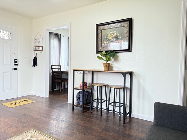 Un salon doté d’un parquet en bois foncé, d’un fauteuil gris, d’une petite table sur laquelle est posée une plante, et d’un tableau encadré accroché au mur.
