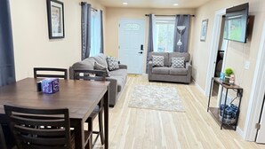 A living room with a sofa, a dining table with chairs, a TV, and a door.