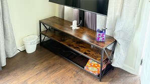 A TV on a wooden stand in a room with patterned curtains and a window.