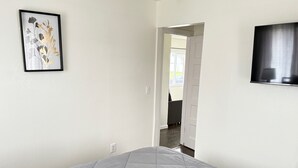 A bedroom with a bed, a framed artwork on the wall, and a TV mounted on the wall.