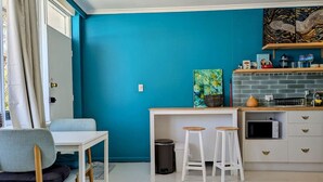A compact kitchen with teal walls, a white countertop, and a small dining area with a chair and table. - Artist’s Studio in Fitzroy North (Fitzroy North)