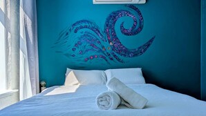 A bed with white linens, a rolled towel, and a teal wall with a decorative swirl pattern. - Artist’s Studio in Fitzroy North (Fitzroy North)