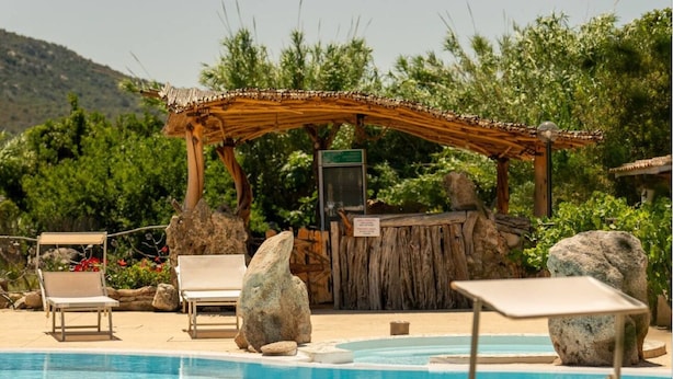 A pool area with lounge chairs, a wooden pergola, and a signboard.