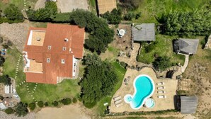 An aerial view of a residential area with a large house, a swimming pool, and surrounding greenery.