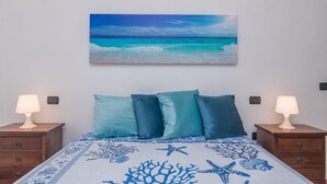 A bedroom with a bed, two nightstands, and a wall-mounted painting of a beach scene.